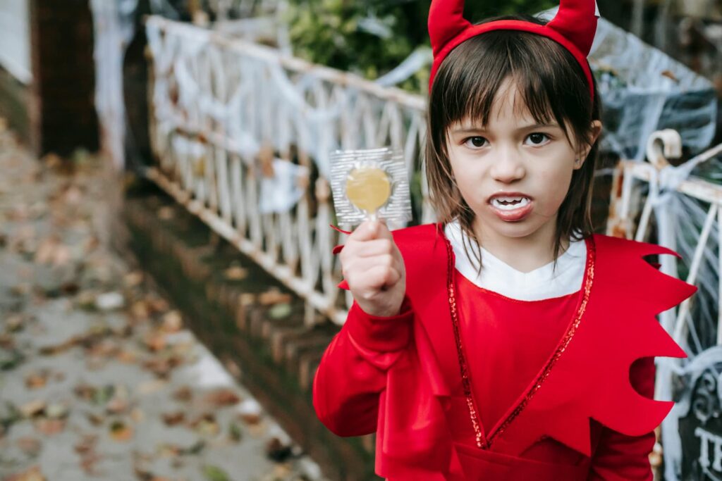 A little girl in a devil costume holding a sucker while trick-or-treating on Halloween