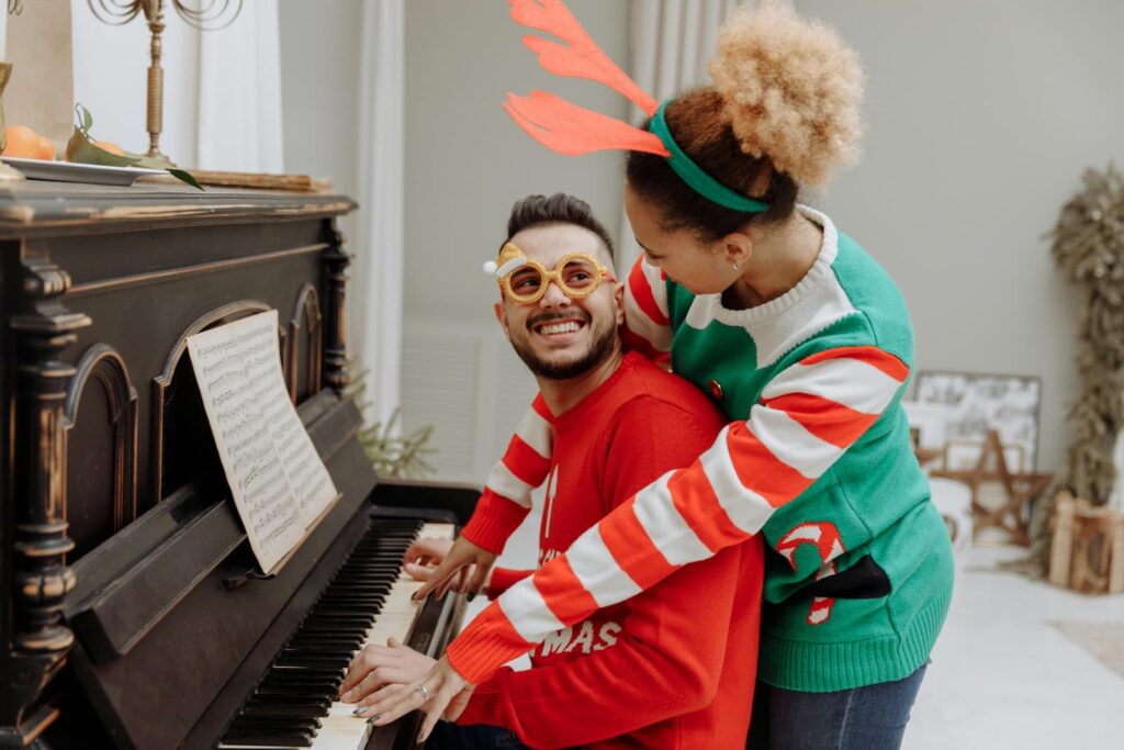 A happy couple wearing Christmas-themed clothes sitting at a piano
