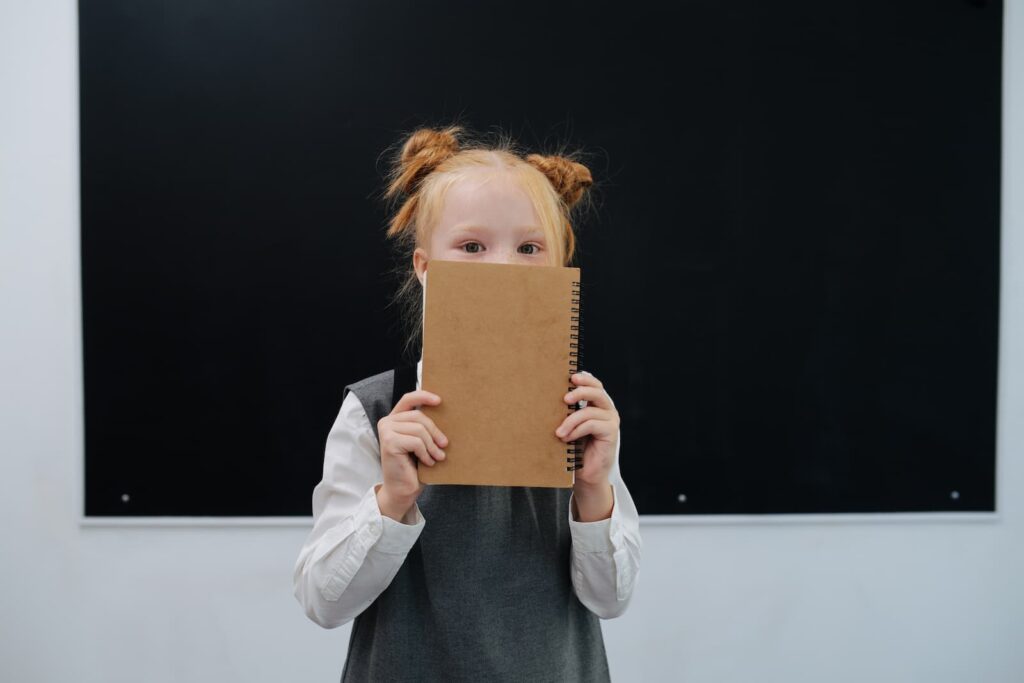 A quiet young girl hiding her face behind a notebook