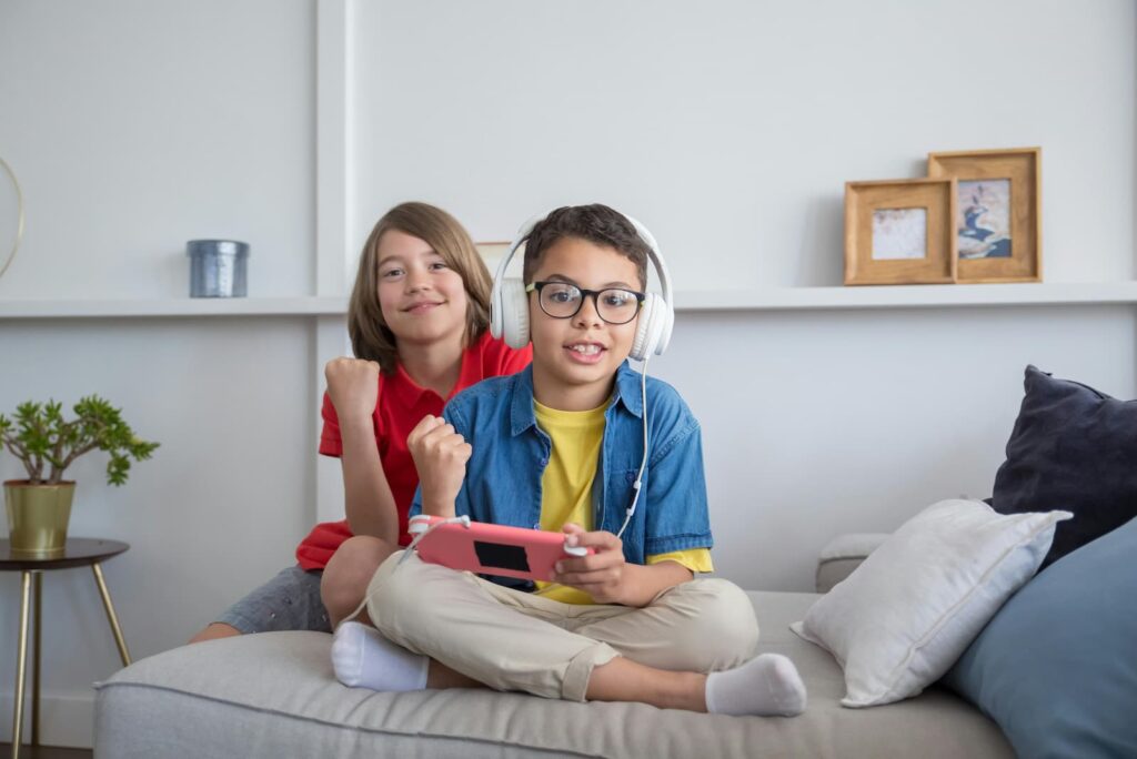 Two young boys playing video games while sitting on a small sofa