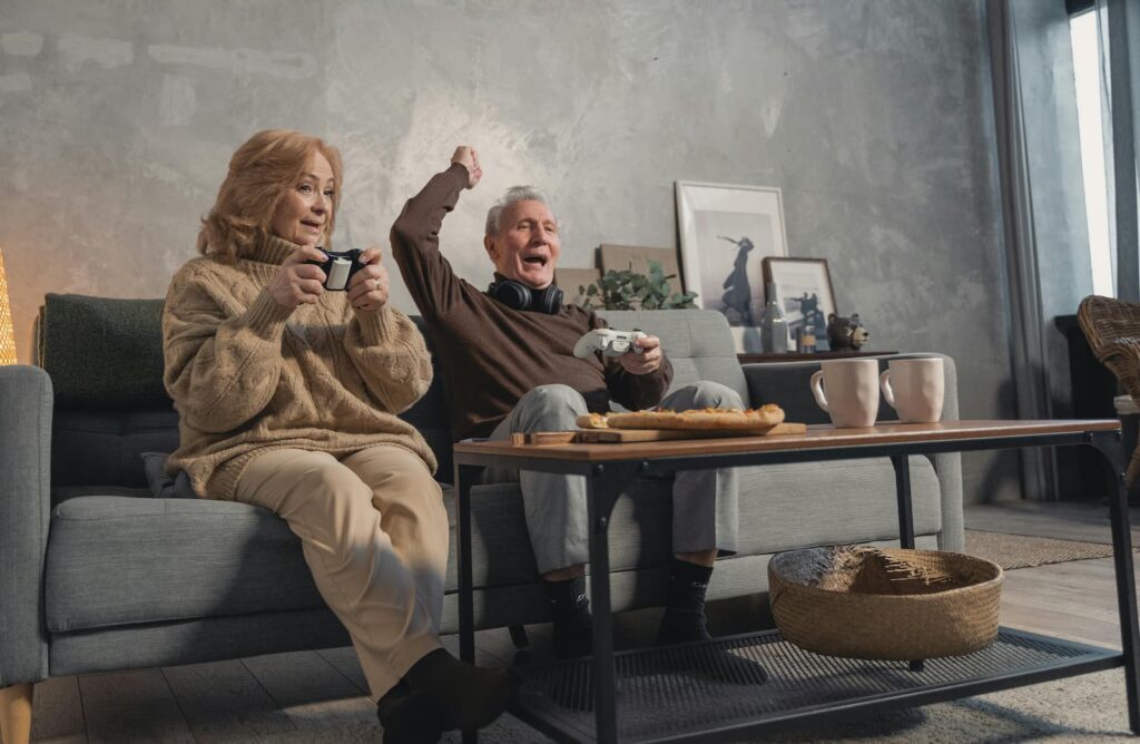An older couple playing video games while sitting on a sofa in their living room