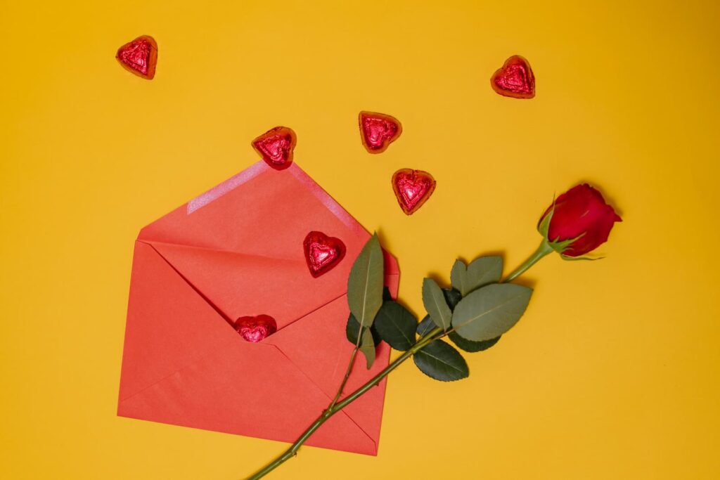 Chocolate candy, a red rose and a red greeting card envelope