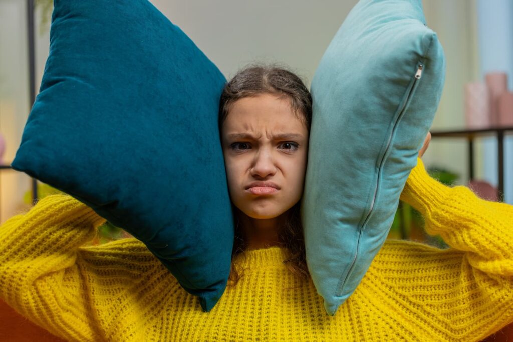 An annoyed girl holding pillows up to her ears