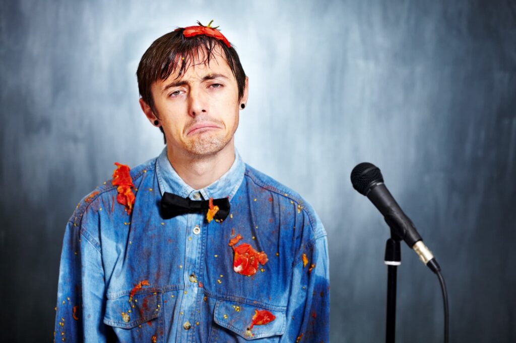 A sad performer standing next to a microphone while covered in smashed tomatoes