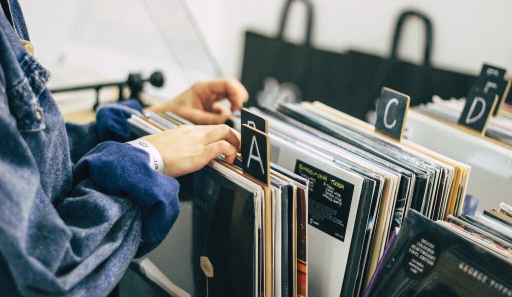 A close-up of a person's hands looking through records in a store's rack