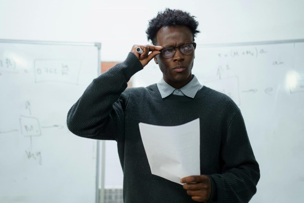 A young man with a confused expression adjusting his glasses