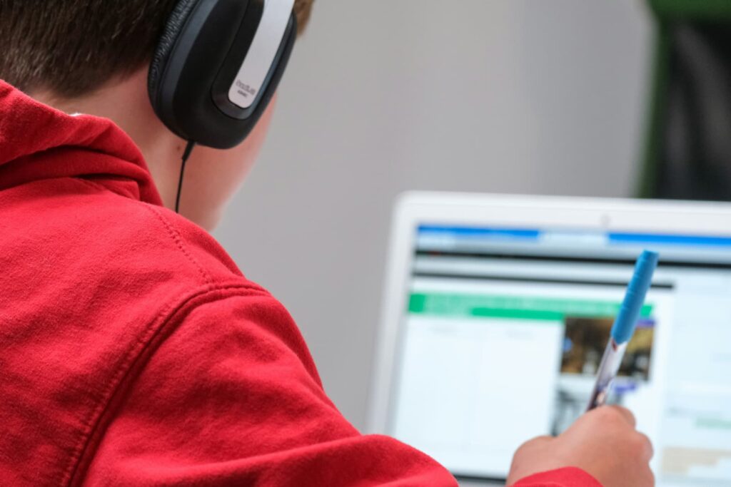 A young student wearing headphones and taking notes during an online lesson