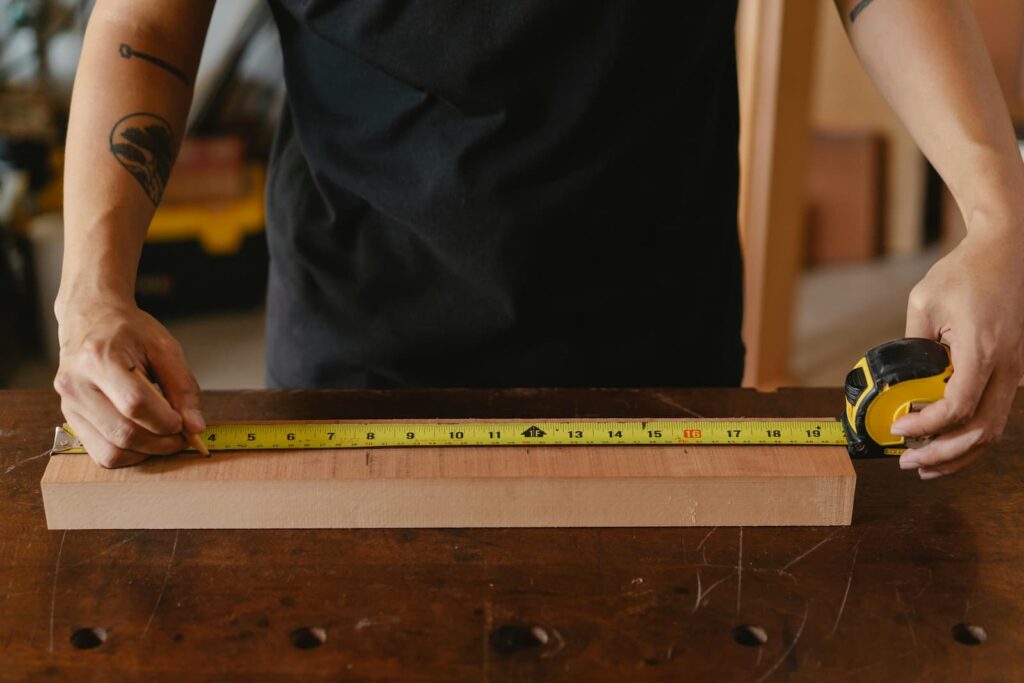 A man using a tape measure while making a mark on a piece of wood