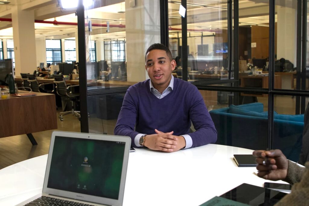 A young professional sitting at a table while being interviewed in an office space