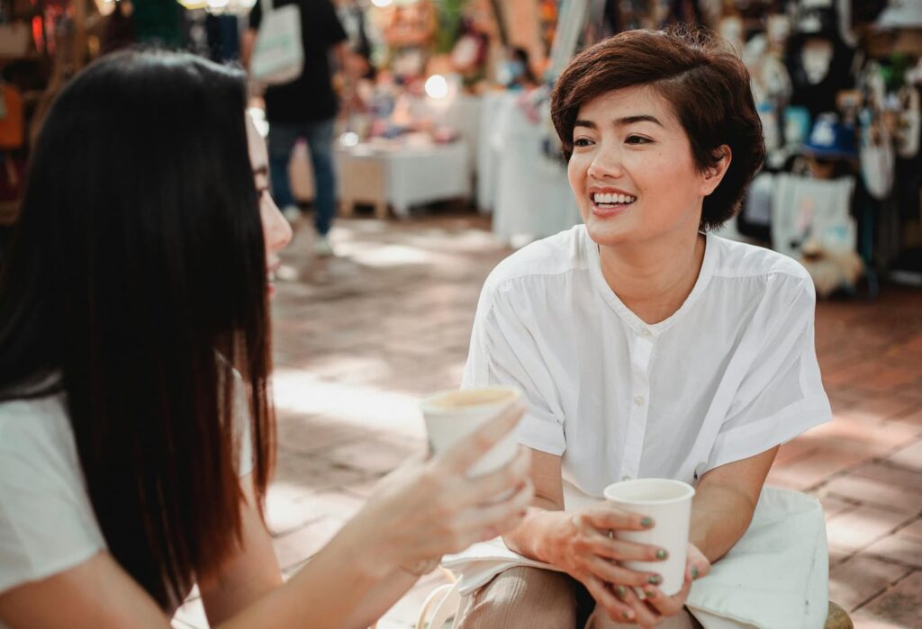 Two seated women talking in a busy marketplace