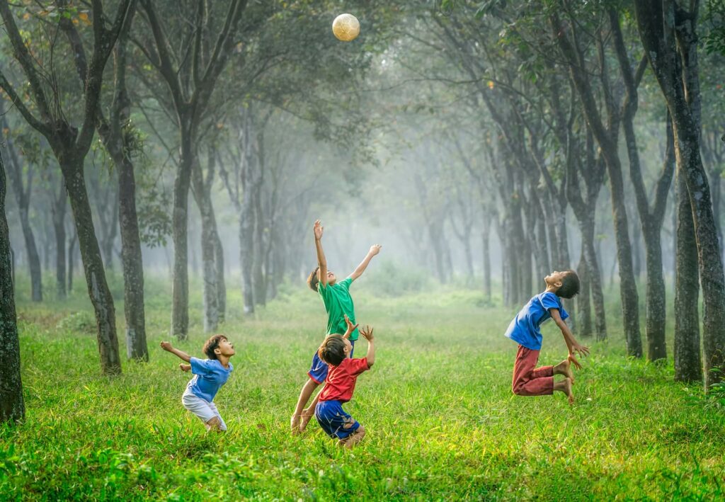 A group of children playing with a ball is a field with trees