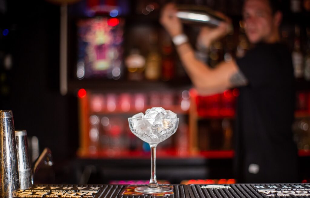 A bartender preparing a drink behind a martini glass filled with ice