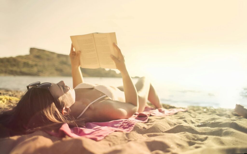 A woman reading a book while lying on the beach