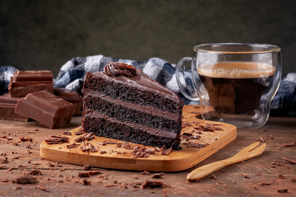 A slice of chocolate cake next to pieces of chocolate and a glass of espresso