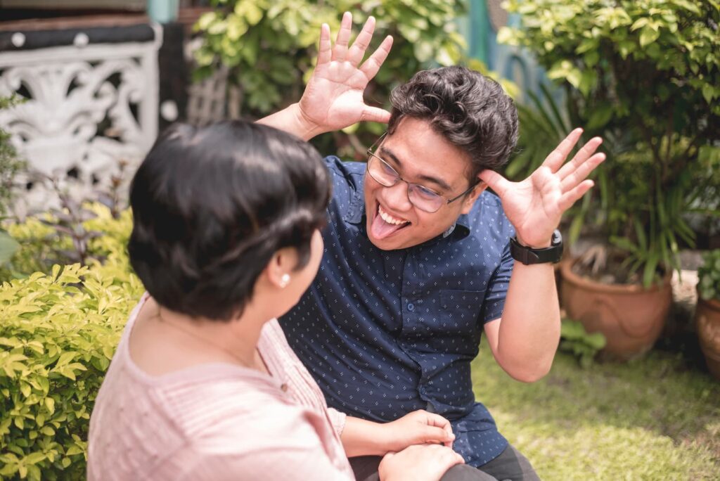A man sticking out his tongue and making a funny face to a woman sitting next to him