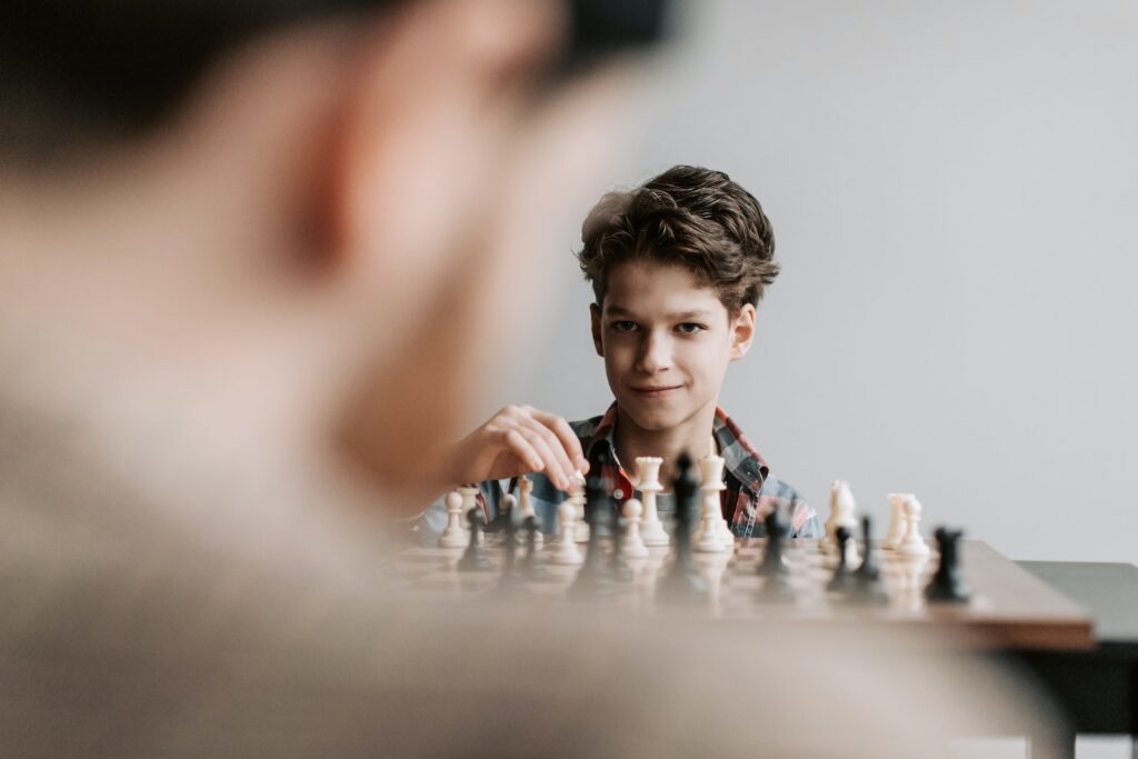 A confident boy playing chess and smiling at his opponent