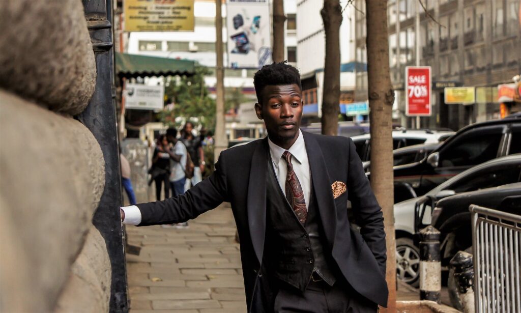 A young, well-dressed man in a dark suit standing on the street