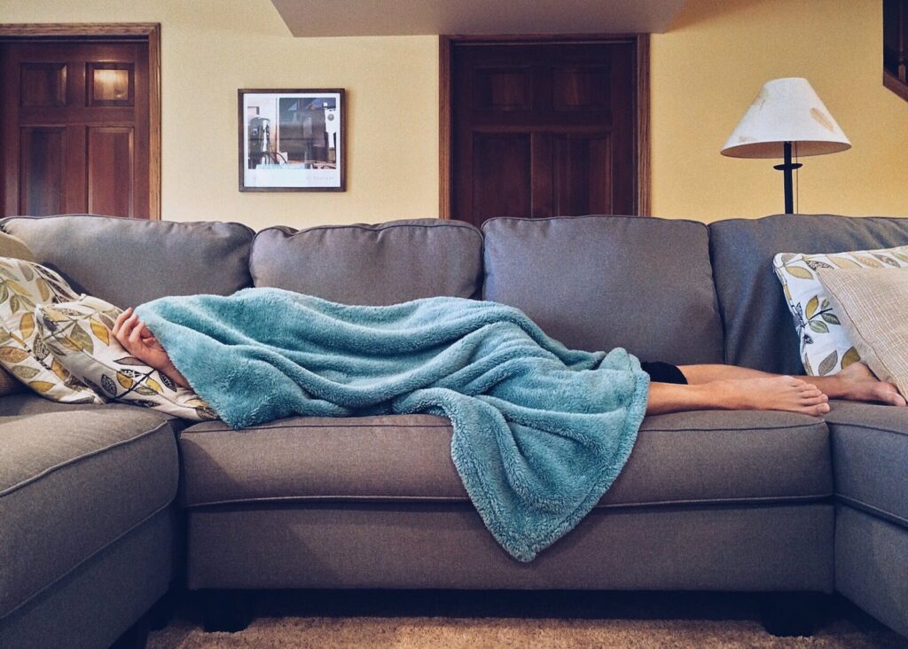 Man sleeping under blanket while lying on a sofa