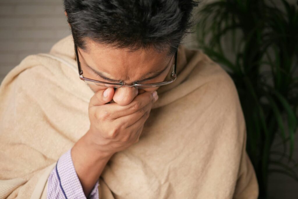 A man wrapped in a blanket and coughing