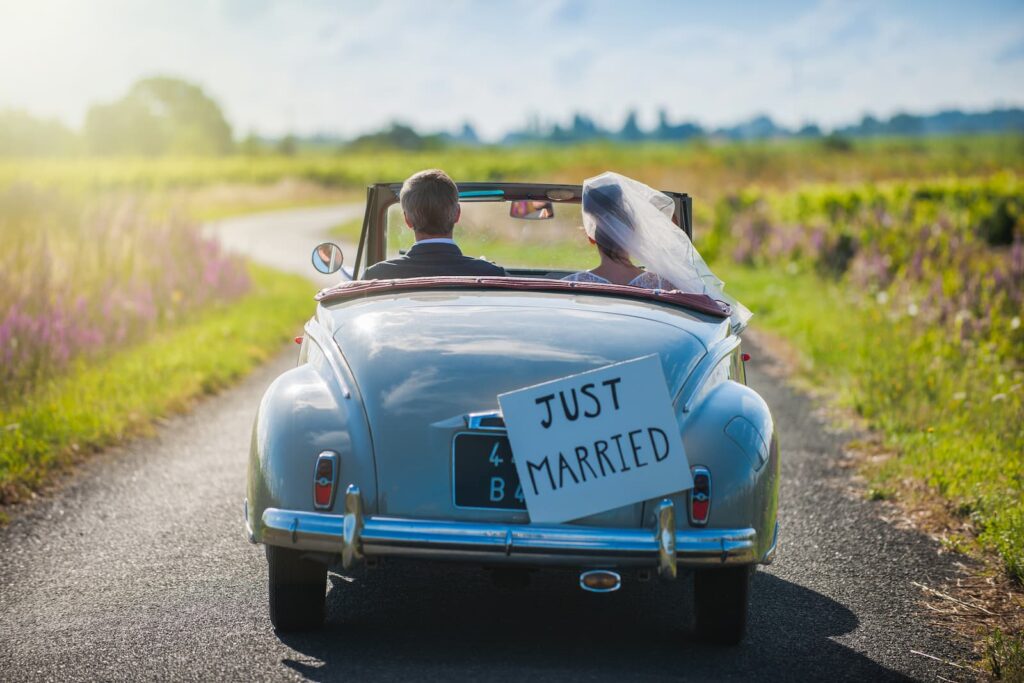 A couple driving down a rural road with a "Just Married" sign on the back of their car