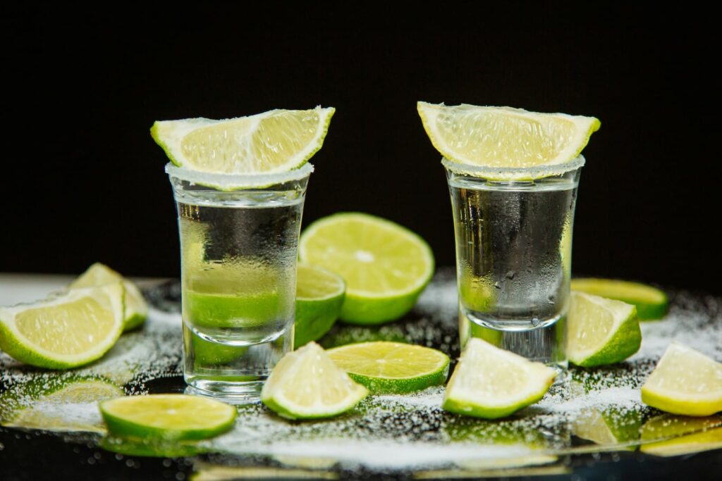 Two full shot glasses surrounded by sliced pieces of lime