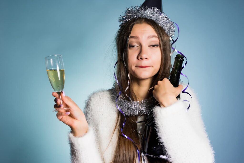An intoxicated woman in a party hat holding a champagne glass and a bottle