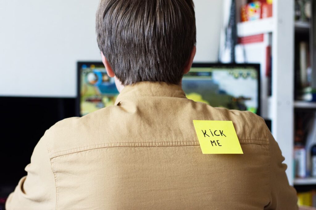 A man with a note stuck to his back that reads "KICK ME"