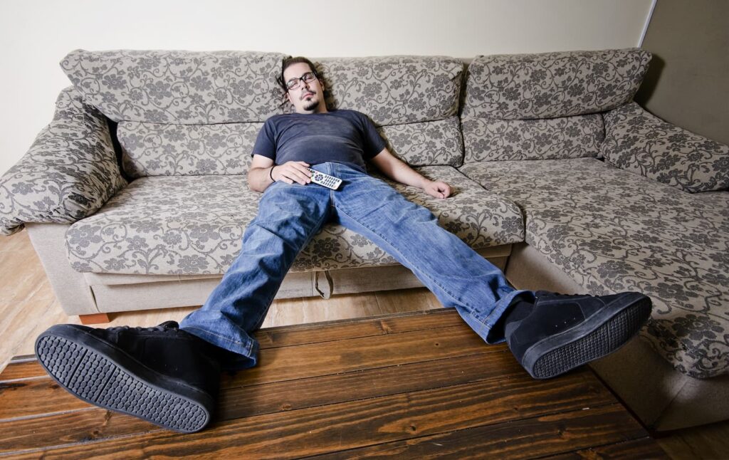 A lazy man sleeping on a sofa while holding a television remote