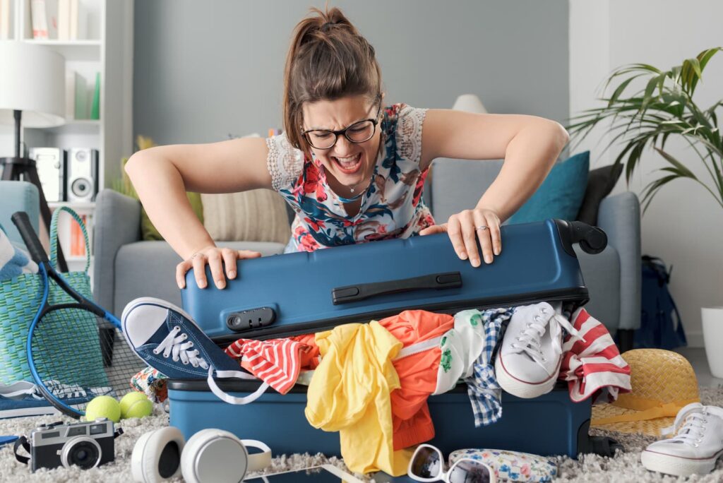 A frustrated woman trying to close a suitcase stuffed with clothes
