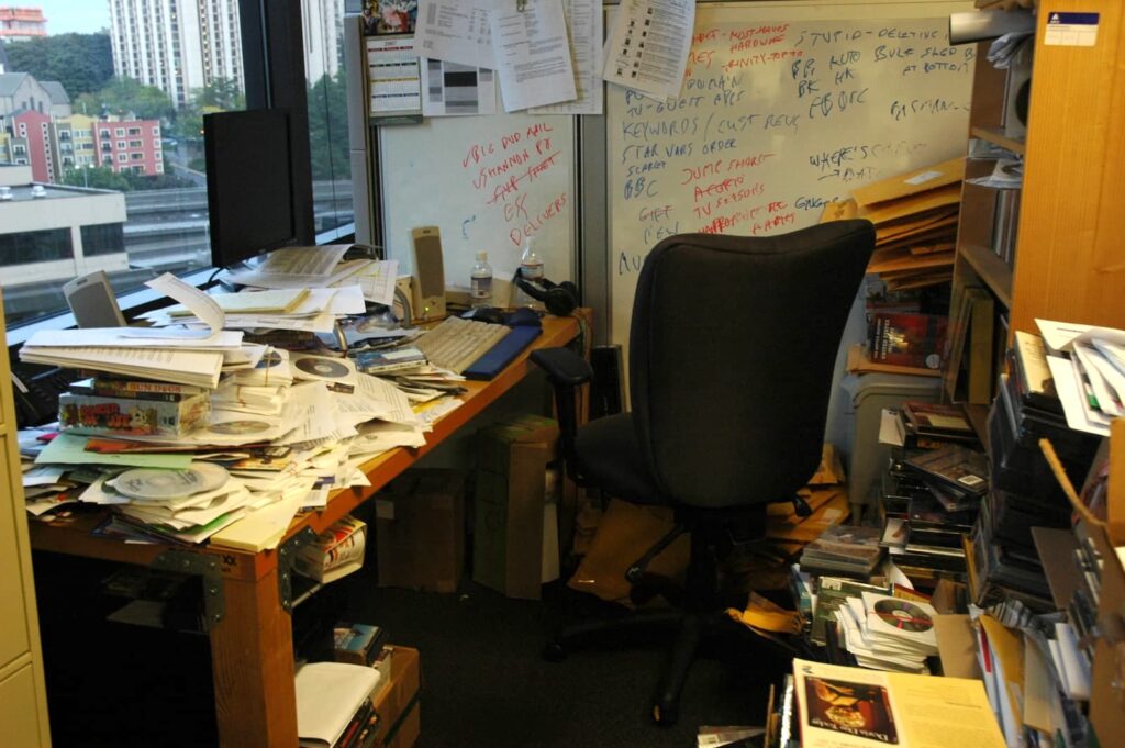 A messy office area with a desk covered in papers and CDs
