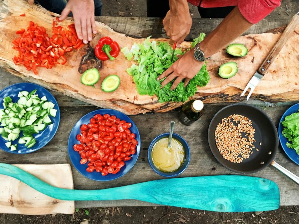 Two people cutting vegetables on a large table covered with plates of ingredients