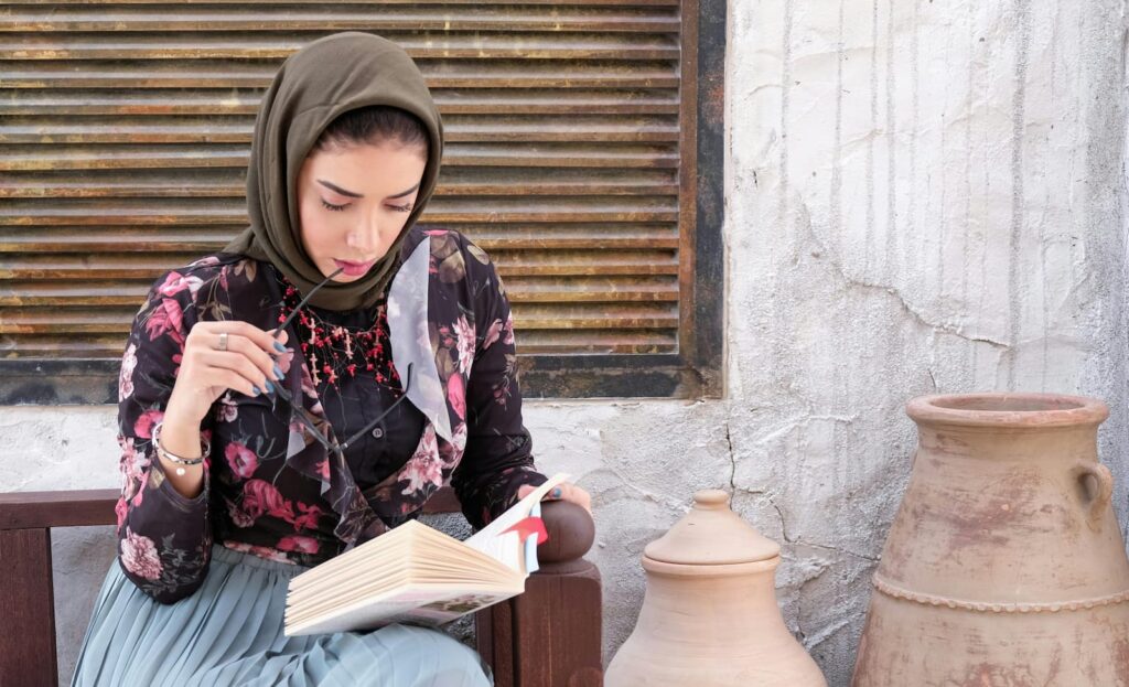 A woman reading a book while sitting on a bench outdoors