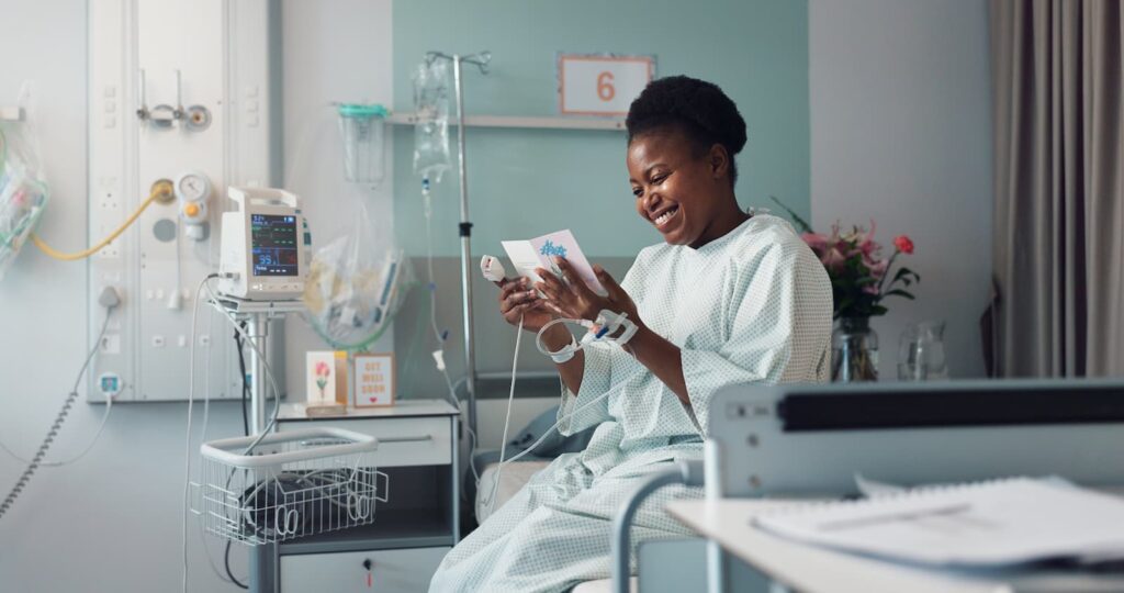 A smiling woman reading a get-well-soon card while sitting on a hospital bed