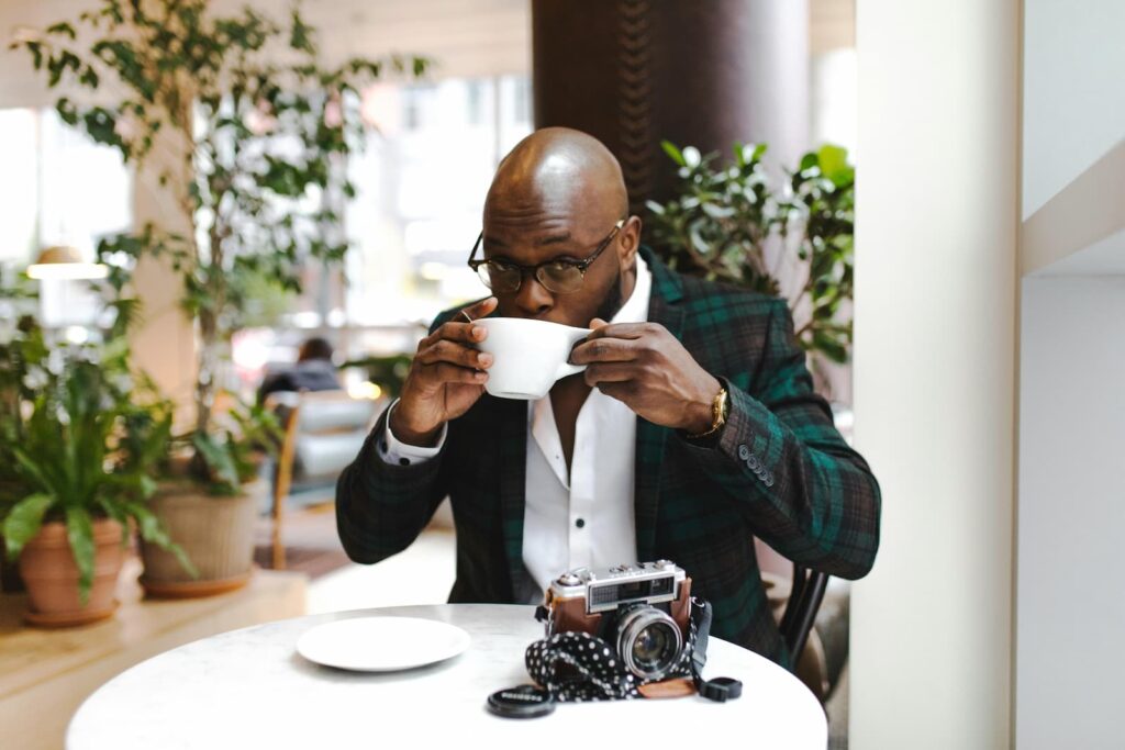 A well-dressed man drinking a cup of coffee while seated at a small table