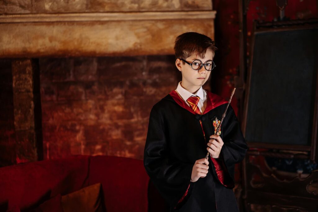 A young boy holding a wand and dressed in a long robe