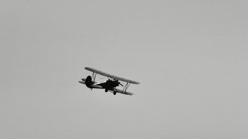 A black and white photo of a biplane flying in the sky