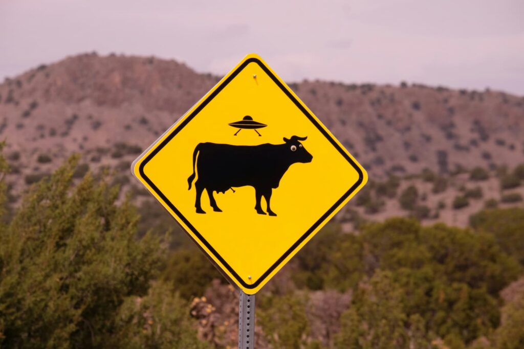 A street sign depicting an alien spaceship flying above a cow