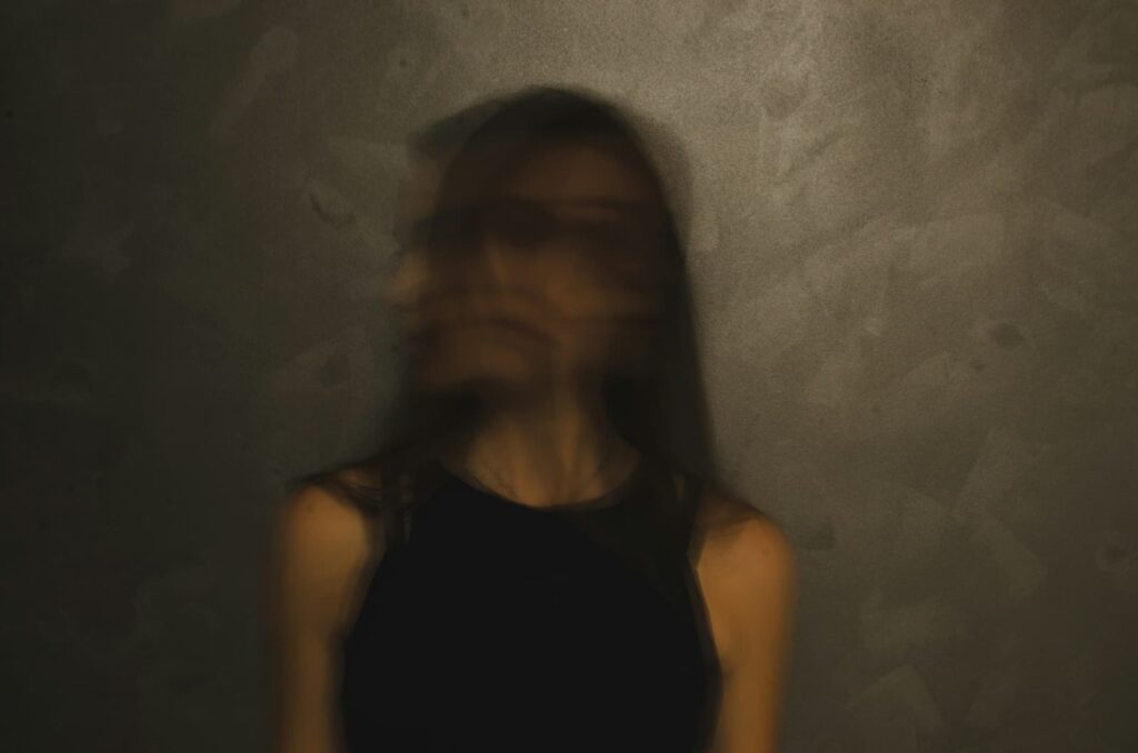A woman with a blurry head and face standing on a dark background