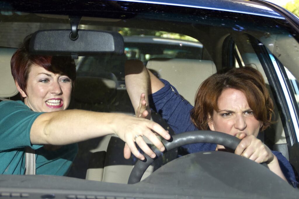 Two annoyed women fighting for control of a car's steering wheel