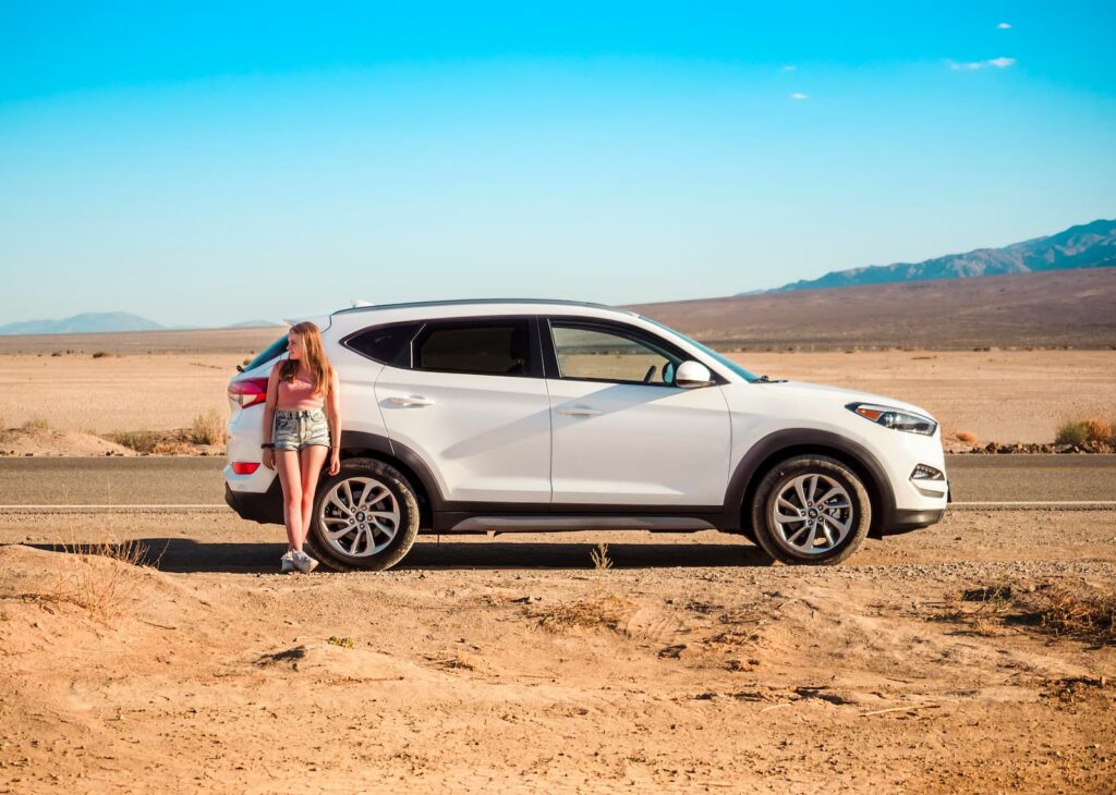 A woman leaning against a rental car in the desert
