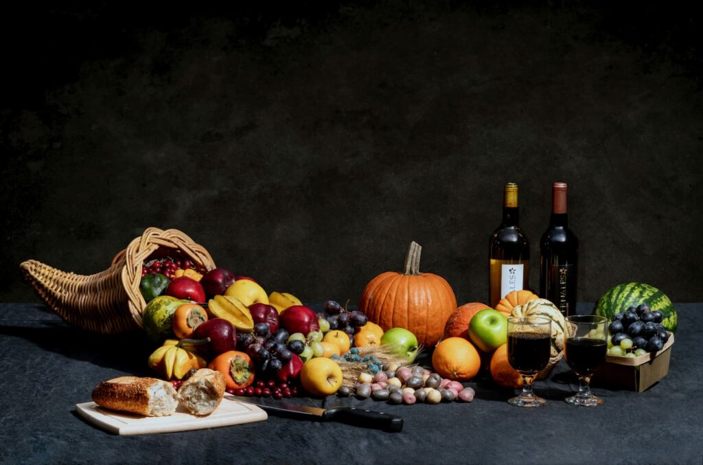 Bread, wine and various fruits displayed with a cornucopia, representing plenty of the fall harvest season