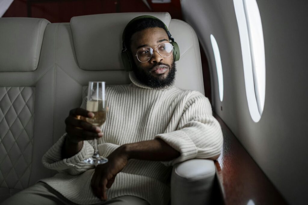 A man with headphones and a glass of champagne sitting in the first section of an airplane