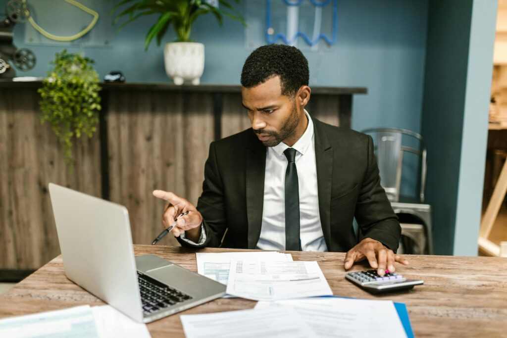 A man sitting at a table with a computer, calculator and various financial documents